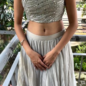 "Grey off-shoulder crop top with shimmering sequins and a flowy pleated skirt."
